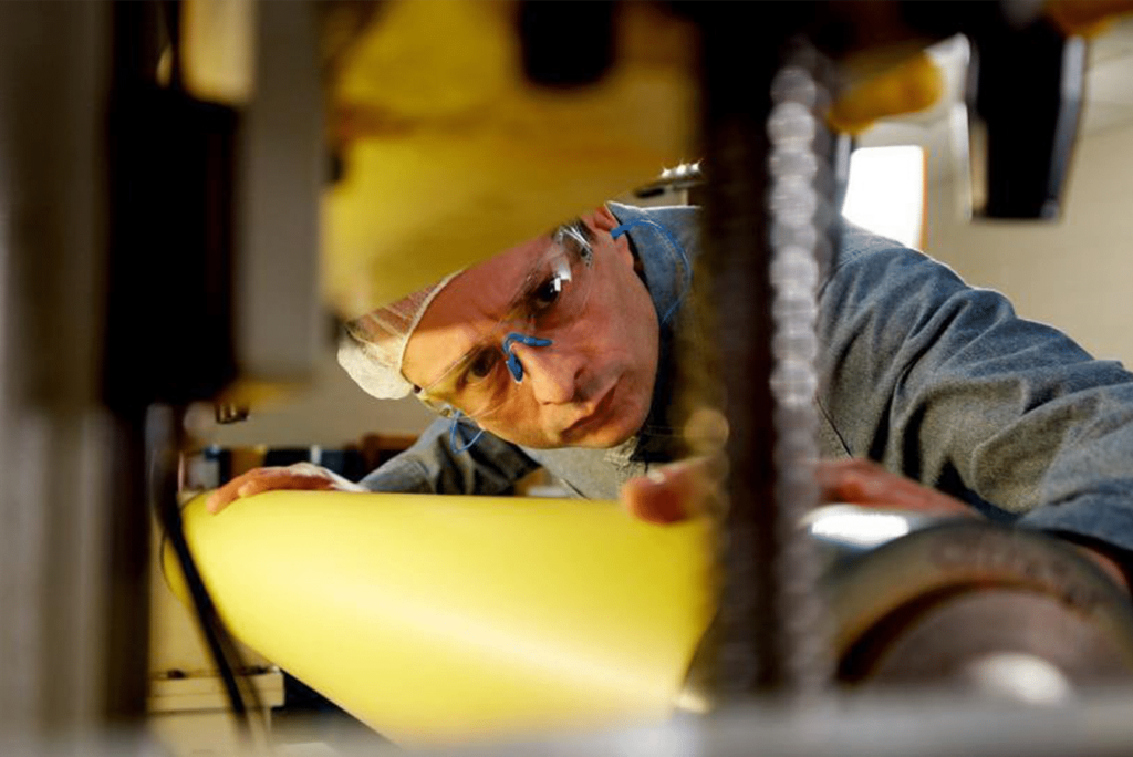 Worker applying 3M mounting tape to a flexographic printing cylinder for secure plate mounting.