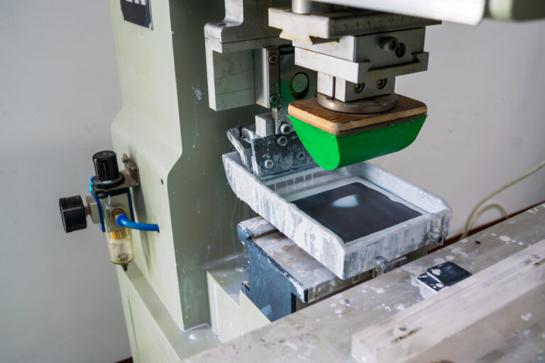 A pad printing machine used to transfer ink from a silicone pad onto a 3D object, with the plate and product securely held in place for precise printing.